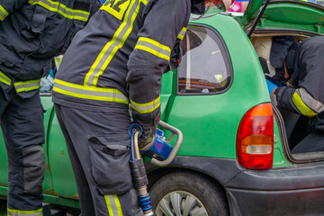 firefighters with hydraulic spreaders for technical and road rescue during exercises and demonstrations next to a damaged passenger car in an accident. Staging