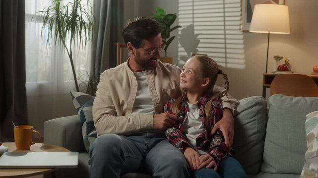 Caucasian family happy parent with kid girl daughter with father relaxing on couch in living room dad touch nose of child hugging cuddling love relationship custody adopted childcare bonding pediatric