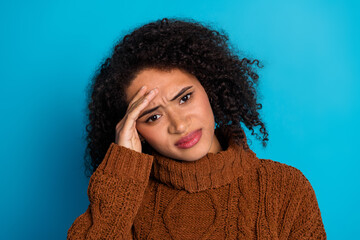 Young woman in brown knit sweater with hand on head expressing confusion against blue background