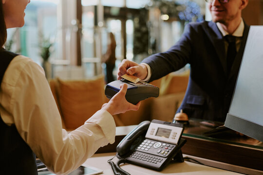 Back view of female receptionist holding wireless payment terminal while hotel guest tapping card