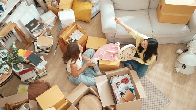 Top view of happy friend unpacking box and picking furniture together. Attractive teenager moving to new apartment while plating talking at living room surrounded with cardboard box. Estate. Myrmidon.