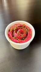 Delicious homemade hummus with baked beetroot sprinkled za'atar in a white plate on a black background