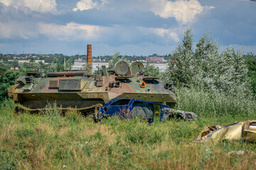 Fototapeta premium Military armored vehicle crushing abandoned passenger car on overgrown grassland near urban city outskirts area