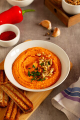 A bowl of red pepper and walnut dip served with bread chips on a plate
