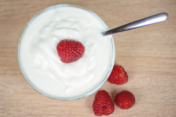 A bowl of yogurt topped with fresh raspberries and a spoon