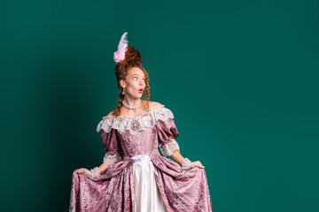 Elegant woman in historical pink dress with red hair, posing against green background, showcasing a...