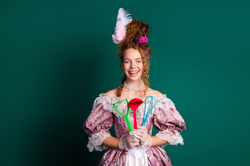 Elegant young woman in vintage pink dress holding colorful kitchen utensils, blending past and...