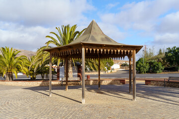 Wooden Gazebo with a Pointed Roof in a Paved Area, Surrounded by Palm Trees
