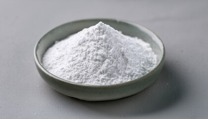 Fine white zinc oxide powder in a bowl on a neutral gray table. Representing its role in medicine and chemical processes.
