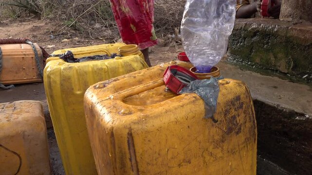 Jerrycans are filled with water at village well in Omo Valley in Ethiopia, water shortage Africa
