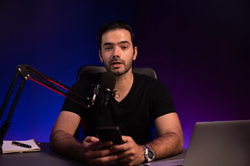 Broadcaster talking to listener on live streaming online, checking message from smartphone on...