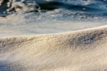 Foamy waves gently roll over a sandy surface, creating a soothing and dynamic composition. The play of light on the foam highlights a serene and natural elegance.