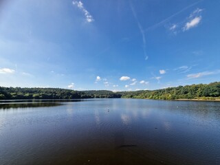 Expansive Blue Sky with Airplane Trails and Cloud Reflections on Reservoir