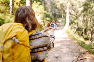Rear view of a young female hiker with a backpack and a compass in her hands against a mountain...
