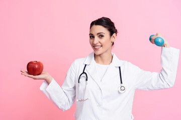 Portrait of smiling female doctor with stethoscope holding red apple and dumbbell isolated.