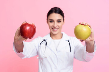 Portrait of smiling female doctor with stethoscope holding red and yellow apples isolated.