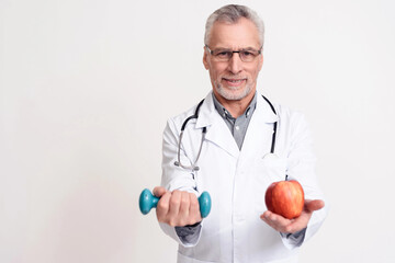 Portrait of doctor with stethoscope holding apple and dumbbell isolated.
