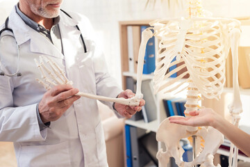 Doctor with stethoscope and female patient in office. Doctor is showing skeleton's hand.