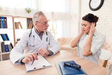 Doctor with stethoscope and female patient in office. Patient's head hurts.