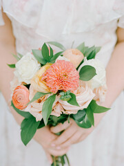 Beautiful wedding bouquet held by a bride featuring soft pastel flowers and green foliage in a natural setting