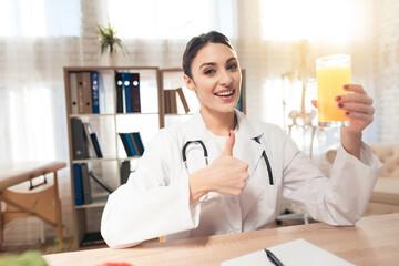 Female doctor sitting at desk in office with microscope and stethoscope. Woman is holding juice.