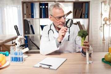 Doctor sitting at desk in office with microscope and stethoscope. Man is giving thumbs up to...
