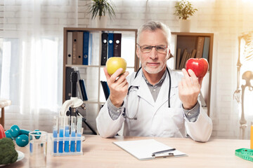 Doctor sitting at desk in office. Doctor is holding fresh red and yellow apples.