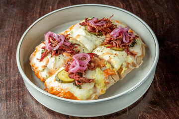  Delicious baked nachos topped with melted cheese, pickles, caramelized onions, and shredded meat, served on a neutral ceramic plate against a wooden background.