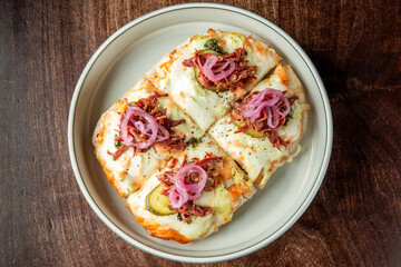  Delicious baked nachos topped with melted cheese, pickles, caramelized onions, and shredded meat, served on a neutral ceramic plate against a wooden background.