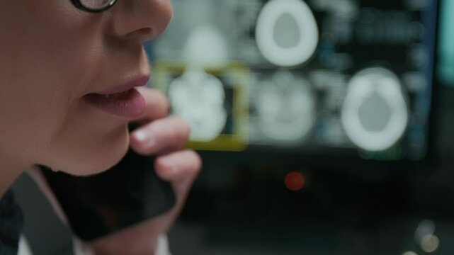 Extreme closeup of lower face and mouth of unrecognizable female radiologist talking on mobile phone to patient, sharing troubling news of brain tomography, MRI scan on computer in blurred background