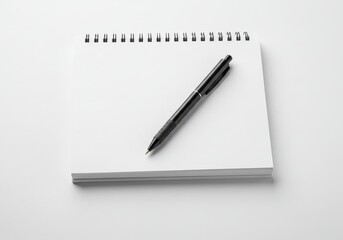 Naklejka premium A spiral bound white notebook with a black pen placed diagonally on top isolated on white background