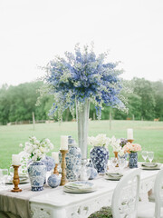 Elegant outdoor dining setup featuring blue floral arrangements and vintage tableware in a serene garden setting