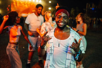 Young man enjoying music festival, showing rock and roll sign with hands
