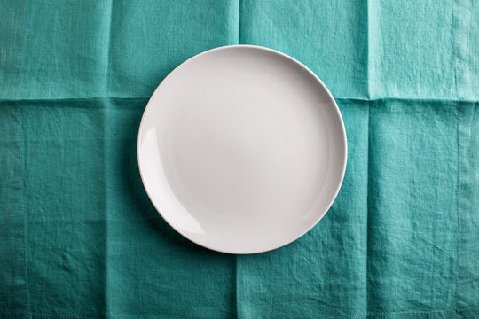 Empty white plate on folded aqua linen overhead

