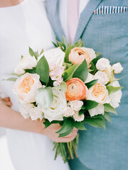 Floral bouquet held by bride and groom during an outdoor wedding ceremony in spring