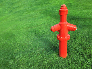 Bright red fire hydrant stands on a freshly mown lawn. Old fire pipe of the city fire extinguishing system against the background of green grass of the lawn. Selective focus, front view. Copy space
