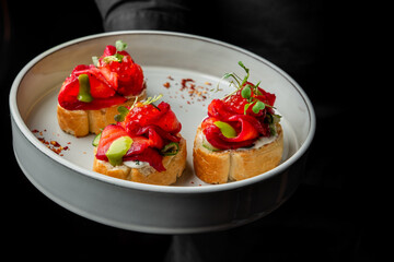 A close-up of a beautifully arranged platter featuring three gourmet canapés topped with colorful vegetables, herbs, and a creamy spread, served on a minimalist white plate.
