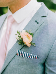 Groom in light gray suit with pink tie and floral accent on a sunny day at an outdoor wedding...