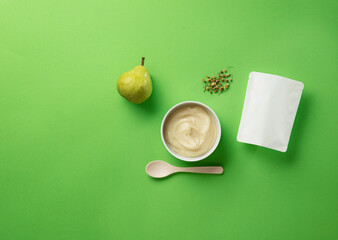 Still life of fruit and vegetables as ingredients of baby food in bowl with spoon and empty packaging.