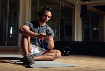 Phone, fitness and headphones with man in gym for streaming, workout podcast and health. Search,...