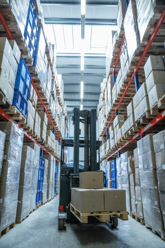 Fork lift in the middle of large warehouse aisle with large pallets of boxes.