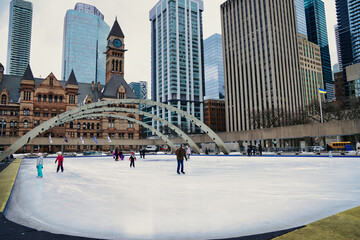 Fototapeta premium Toronto residents enjoy skating on the ice rink at the Nathan Phillips square,with the Old City Town Hall during winter in Toronto,Ontario,Canada 