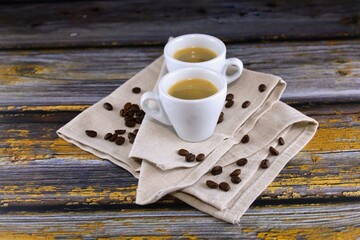 Two cups of espresso and roasted coffee beans on a wooden table. 