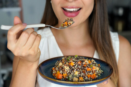 Unidentified girl eating a warm quinoa salad with carrots, broccoli and chickpeas. Focus on the fork.