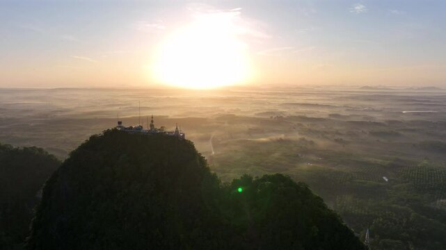 Large golden Buddha statue atop a tall limestone mountain at the Tiger Cave Temple complex in Krabi, Thailand at sunrise (Aerial 4K drone video)