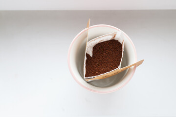 Drip bag in a ceramic cup on windowsill. Instant freshly brewed alternative filter drink in mug. Easy brew black coffee method for home, travel or office. cozy trendy lifestyle