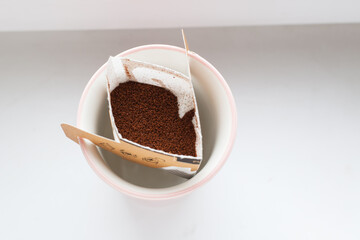 Drip bag in a ceramic cup on windowsill. Instant freshly brewed alternative filter drink in mug. Easy brew black coffee method for home, travel or office. cozy trendy lifestyle