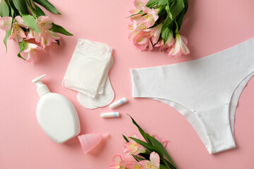 Feminine hygiene products including sanitary pads, tampons, menstrual cup, and white underwear on a pink background with flowers © photoguns