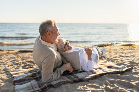 Senior mature couple sitting on beach hugging enjoying outdoor recreation. Old husband wife embracing with tenderness love enjoying sweet bonding. Grandmother grandfather together. Family moment love