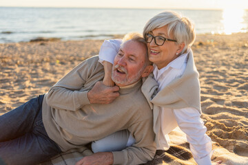 Obraz premium Senior mature couple sitting on beach hugging enjoying outdoor recreation. Old husband wife embracing with tenderness love enjoying sweet bonding. Grandmother grandfather together. Family moment love